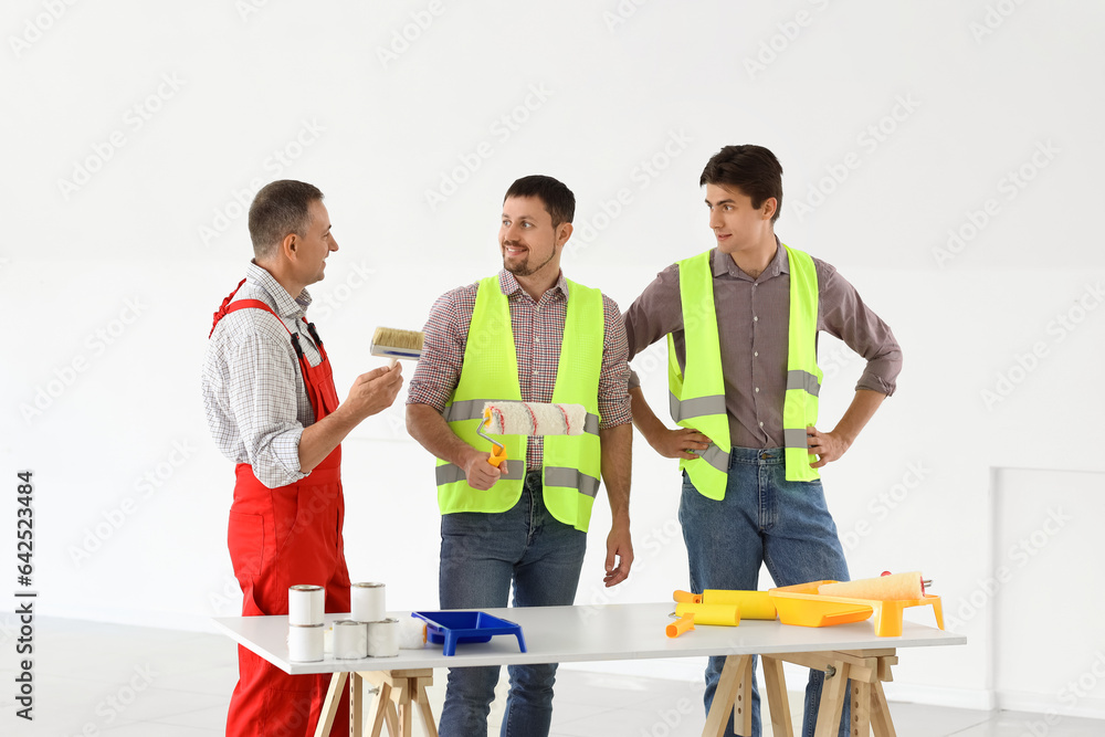 Team of male builders with paint rollers working in room