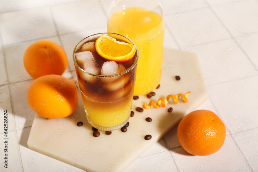 Glass of tasty orange espresso and bottle with juice on white tile background