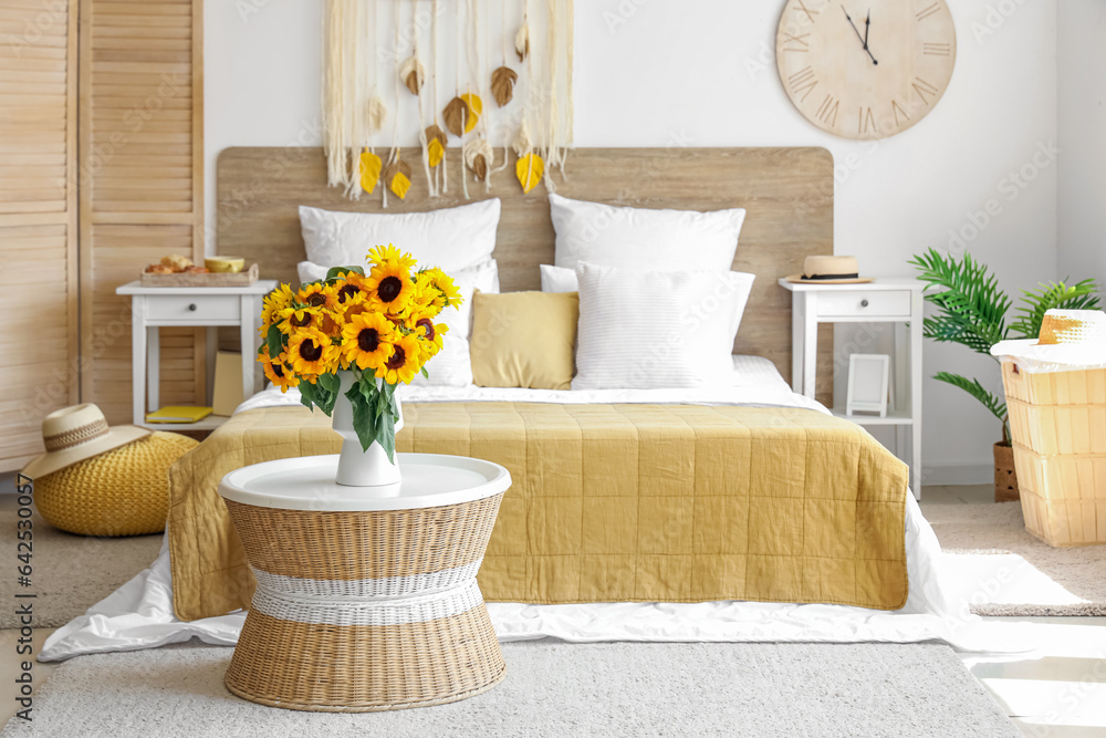 Interior of light bedroom with sunflowers in vase on table