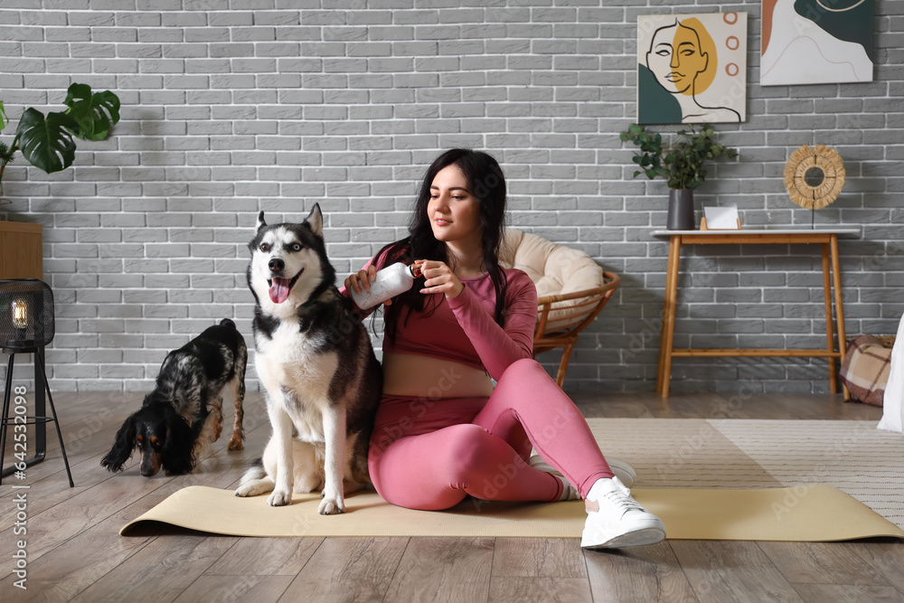 Sporty young woman with bottle of water and her dogs at home