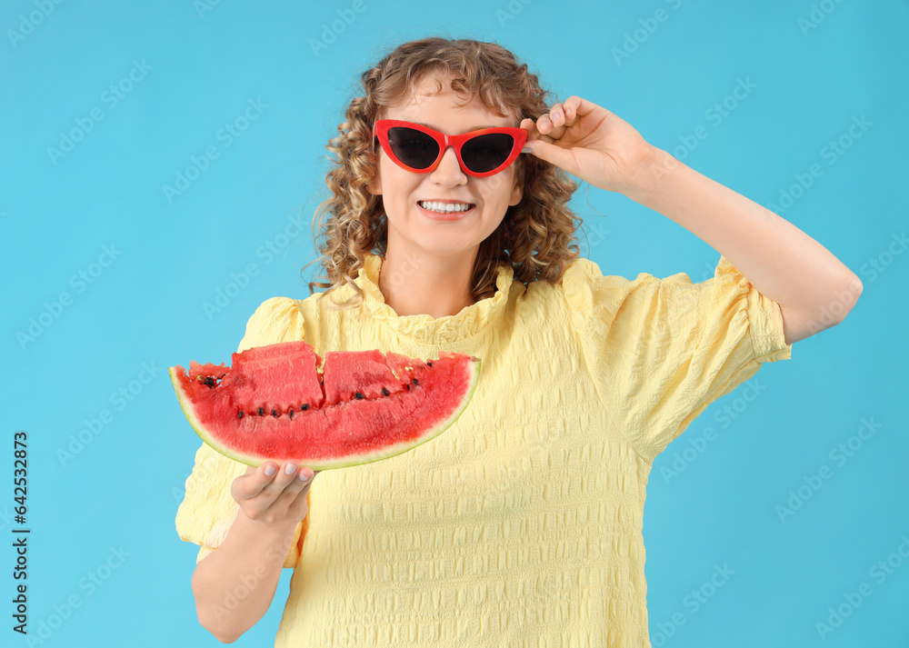 Happy beautiful young woman in sunglasses with slice of fresh watermelon on blue background