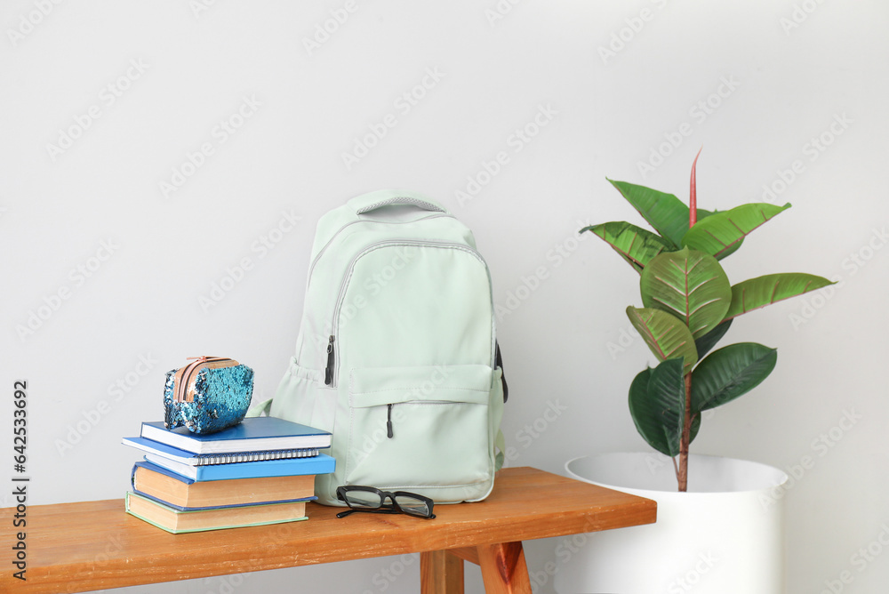 School backpack, stationery, eyeglasses and houseplant on wooden table near light wall