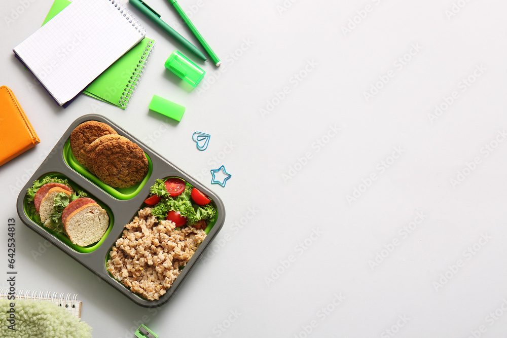 Lunchbox with delicious food and different stationery on white background