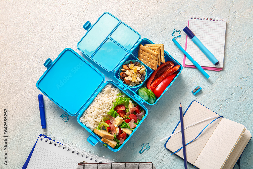 Lunchboxes with delicious food and different stationery on gradient background