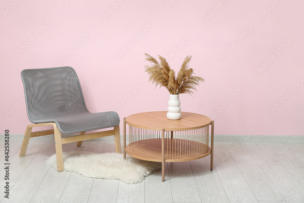 Comfortable armchair and wooden table with pampas grass near pink wall