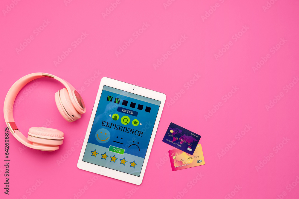 Tablet computer with experience survey, headphones and credit cards on pink background