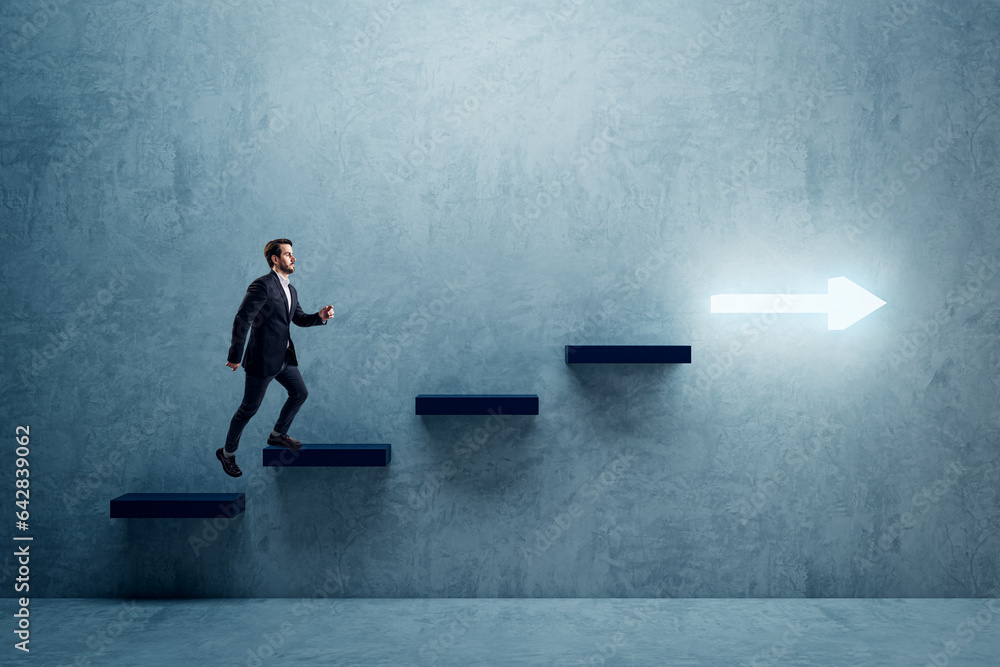 Side view of young business man climbing illuminated arrow stairs to success on concrete wall backgr