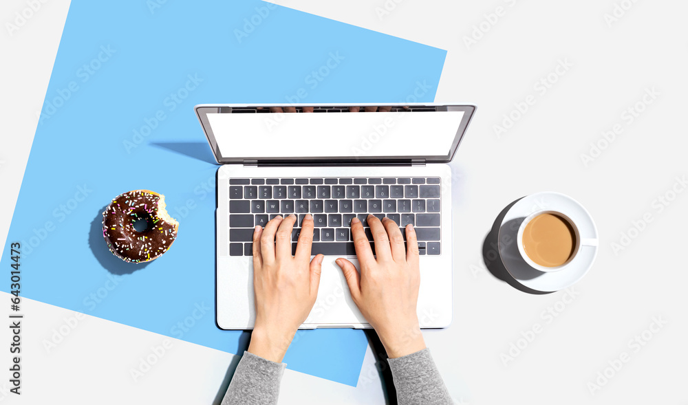 Person using a laptop computer with a donut and a cup of coffee - Flat lay