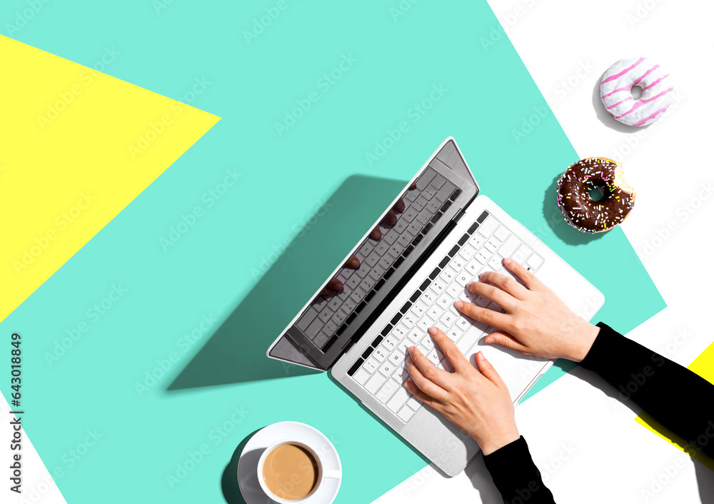 Person using a laptop computer with a donut and a cup of coffee - Flat lay