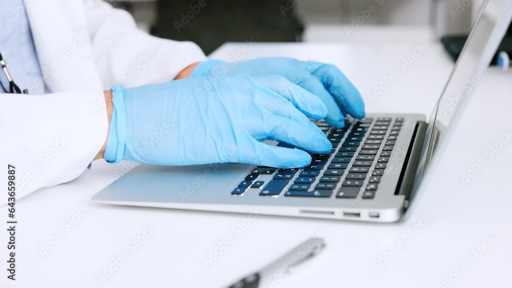 Hands of a scientist in surgical gloves, typing on a laptop in a medical lab. Closeup of a healthcar