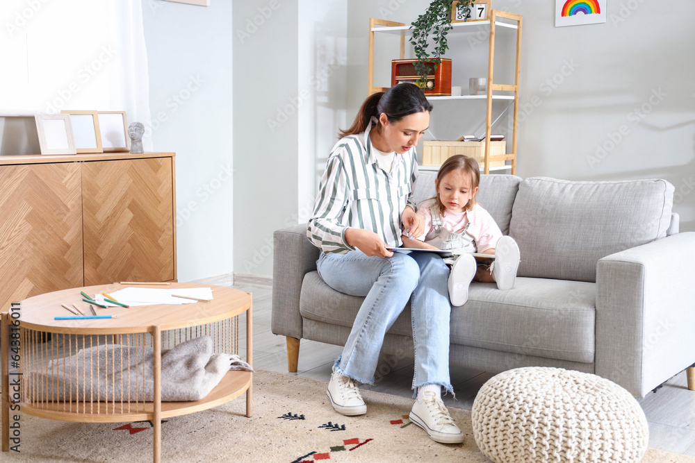 Young woman reading story to her little daughter at home