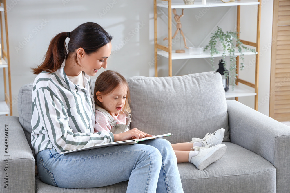 Young woman reading story to her little daughter at home