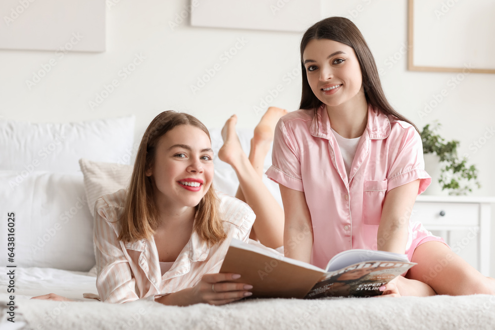 Female friends reading magazine in bedroom