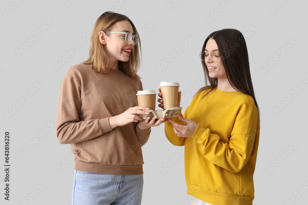 Female friends with cups of coffee on light background