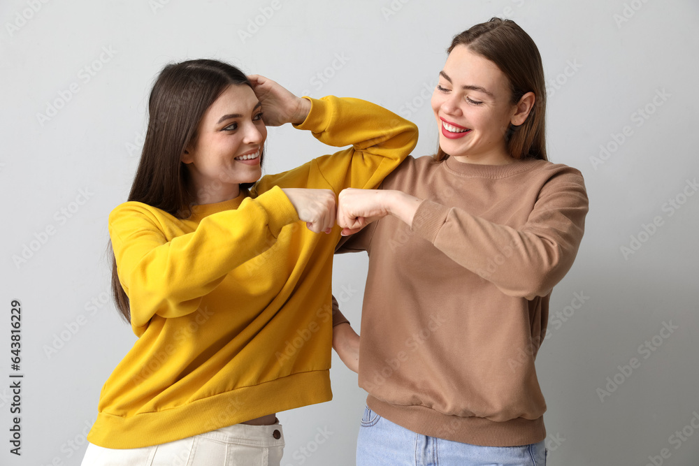 Female friends bumping fists on light background