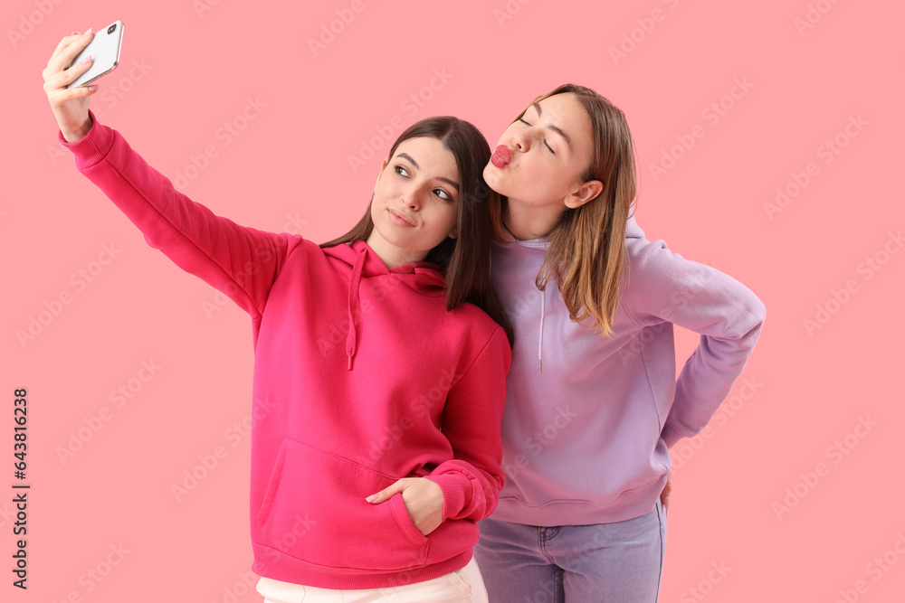 Female friends with mobile phone taking selfie on pink background