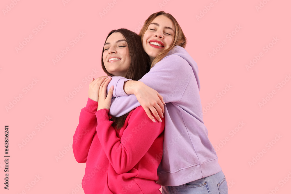 Female friends hugging on pink background