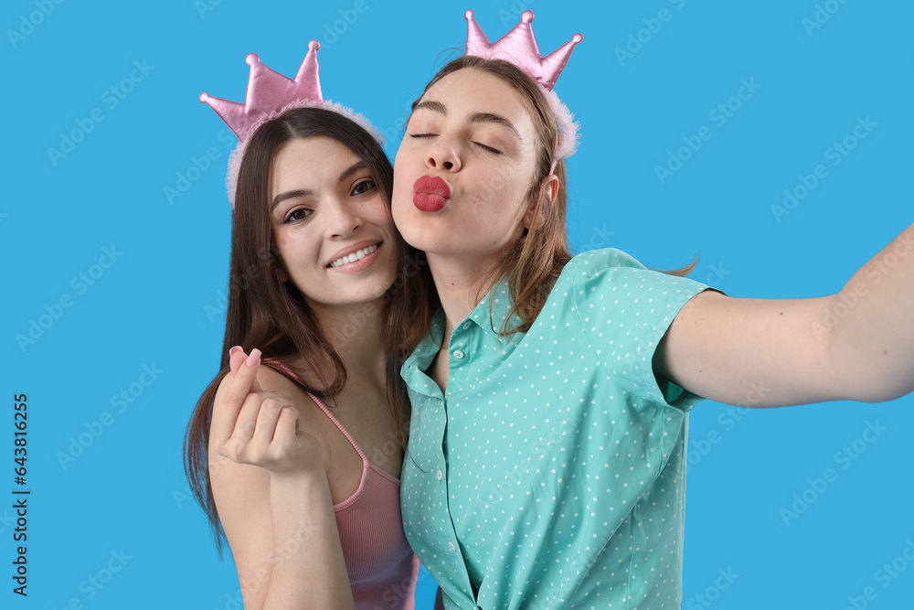 Female friends in crowns taking selfie on blue background