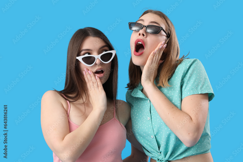 Shocked female friends in sunglasses on blue background