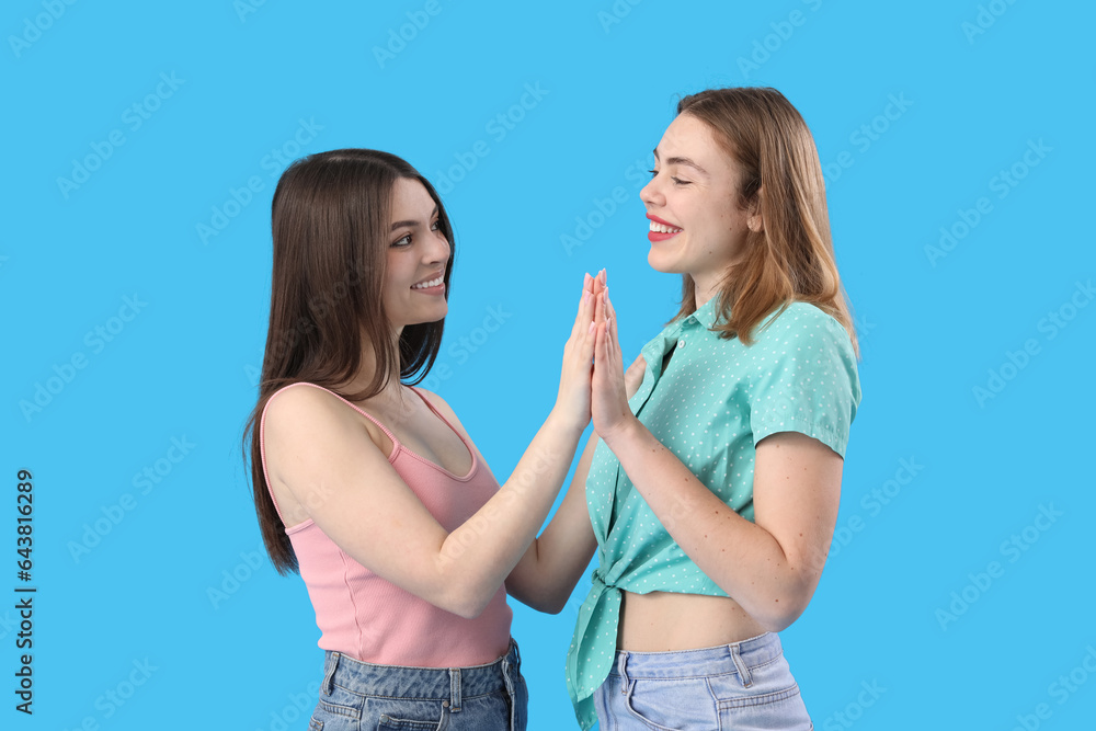 Female friends holding hands on blue background