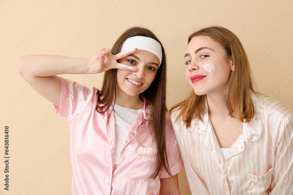 Female friends in pajamas with cream on beige background