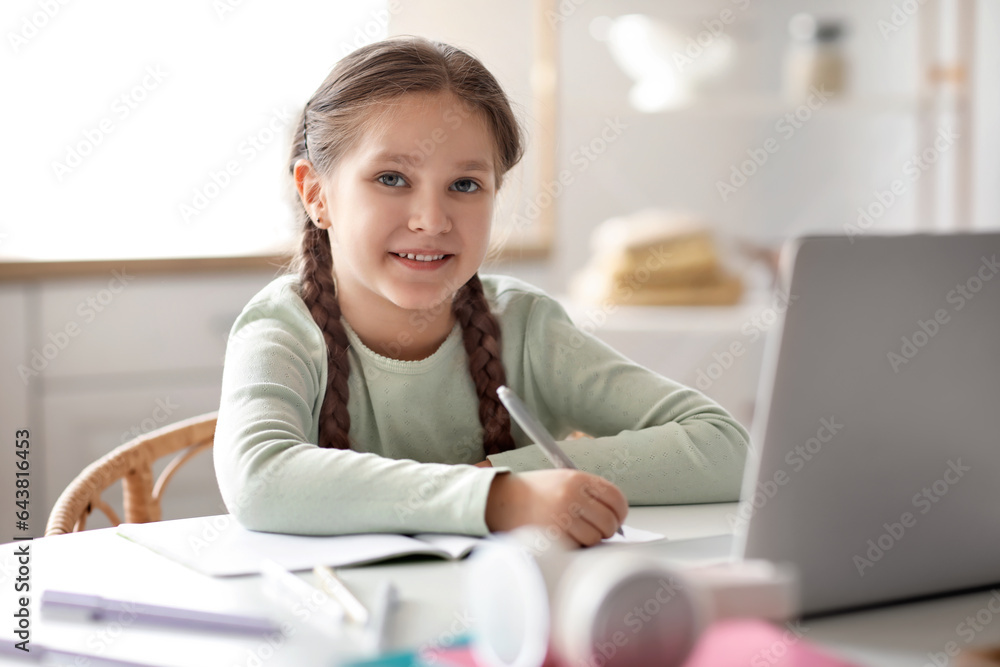 Little girl with laptop studying computer sciences online in kitchen