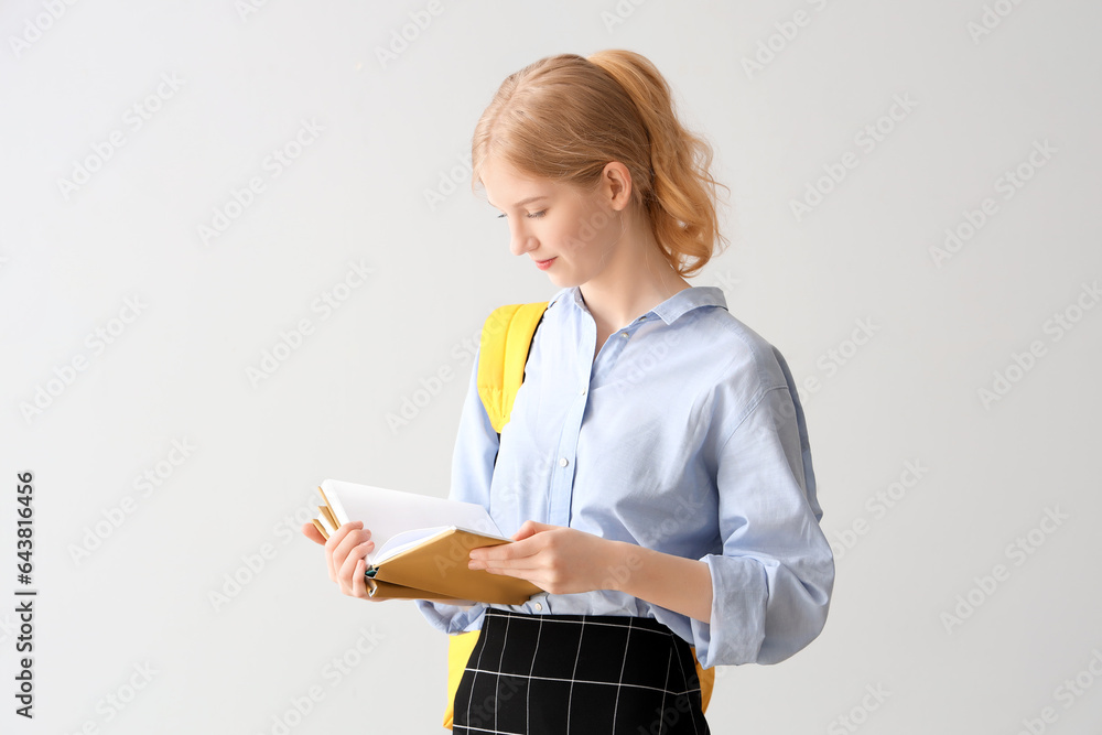 Female student with backpack reading book on grey background