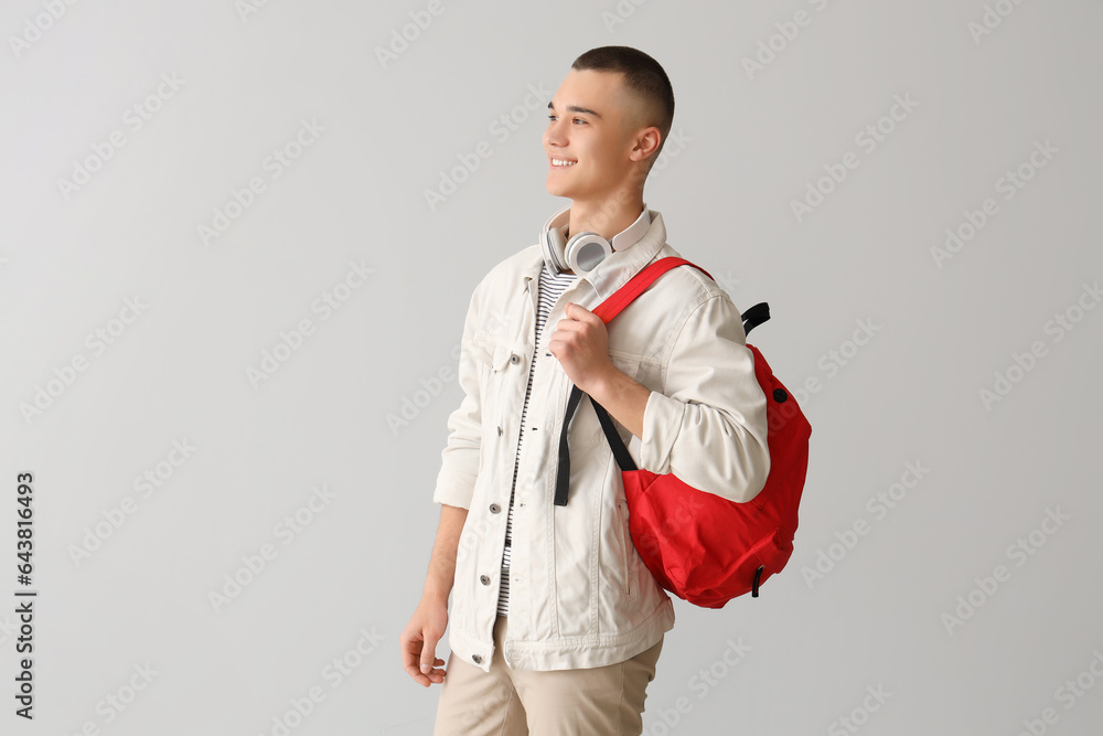 Male student with backpack and headphones on grey background