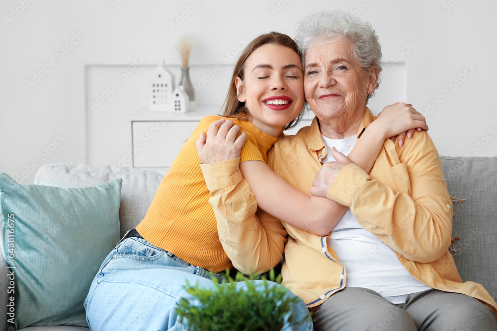 Young woman with her grandmother hugging on sofa at home