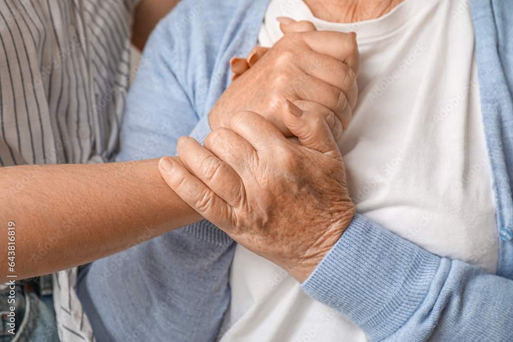 Young woman with her grandmother holding hands at home, closeup