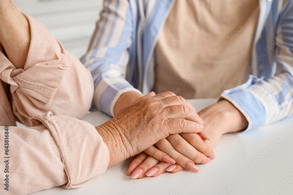 Young woman with her grandmother holding hands at table in kitchen, closeup