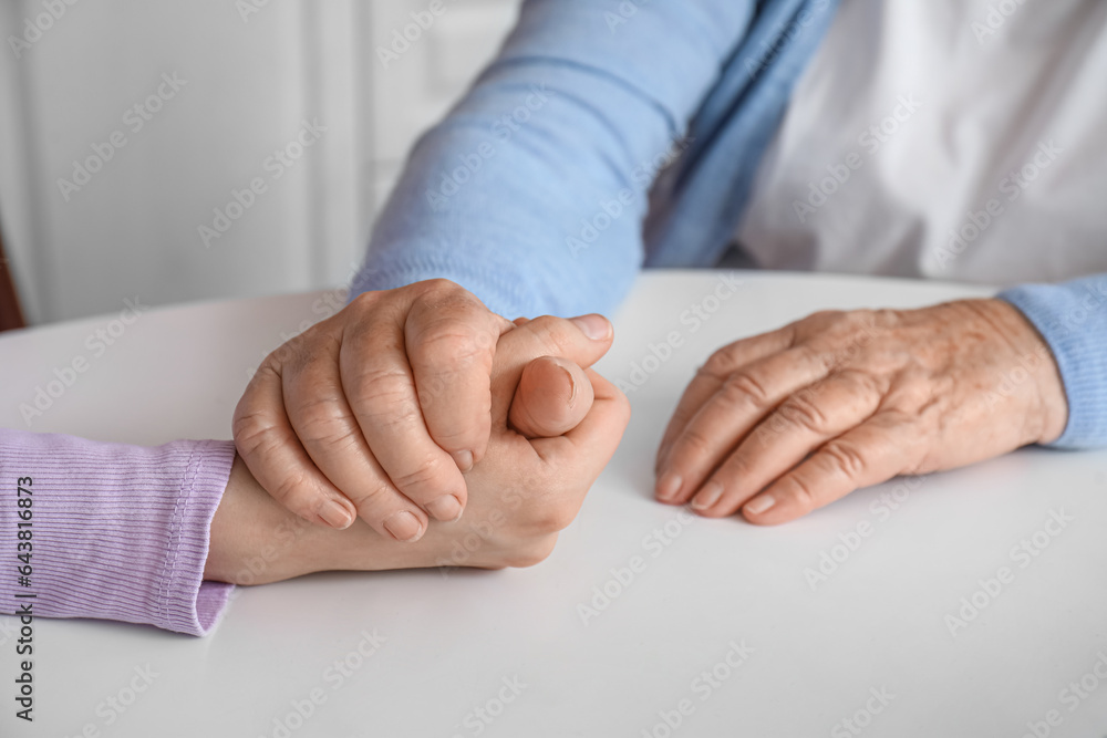 Young woman with her grandmother holding hands at table in kitchen, closeup