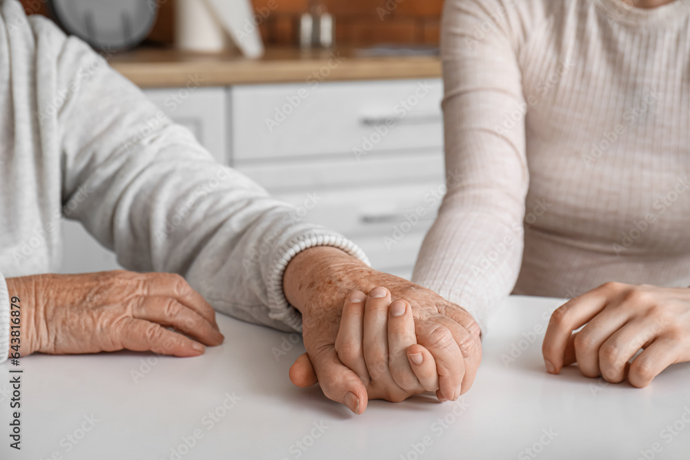 Young woman with her grandmother holding hands at table in kitchen, closeup