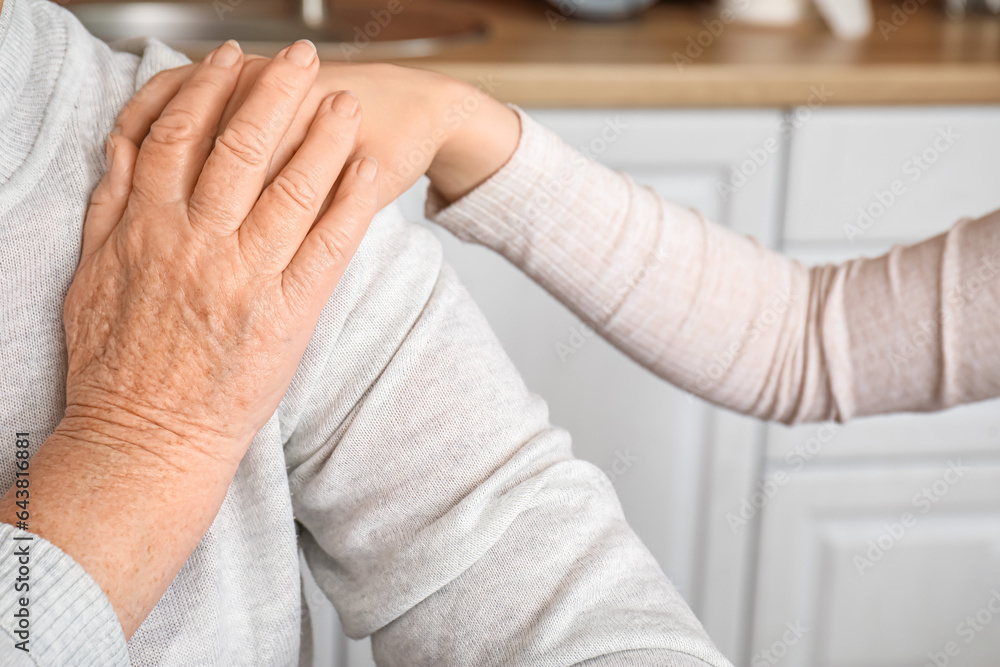 Young woman with her grandmother holding hands in kitchen, closeup