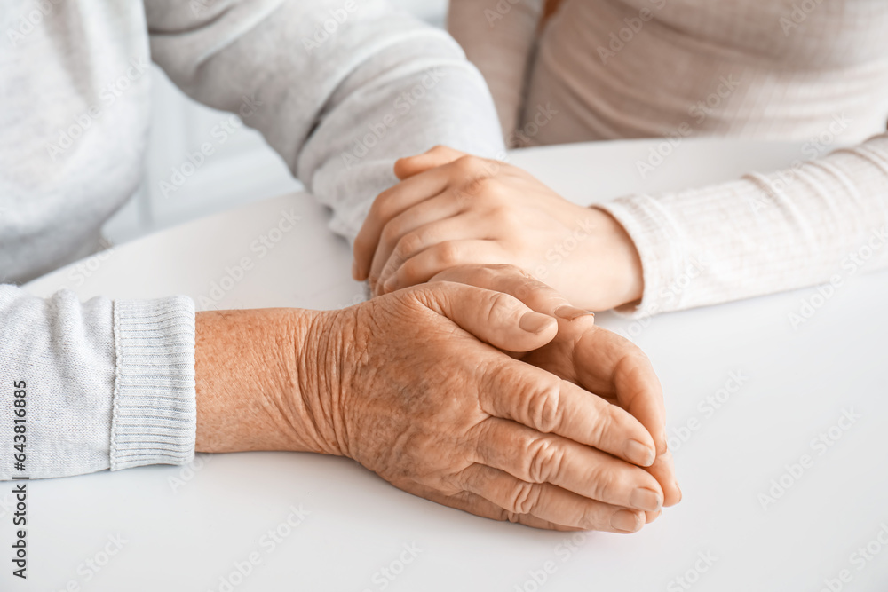 Young woman with her grandmother holding hands at table in kitchen, closeup