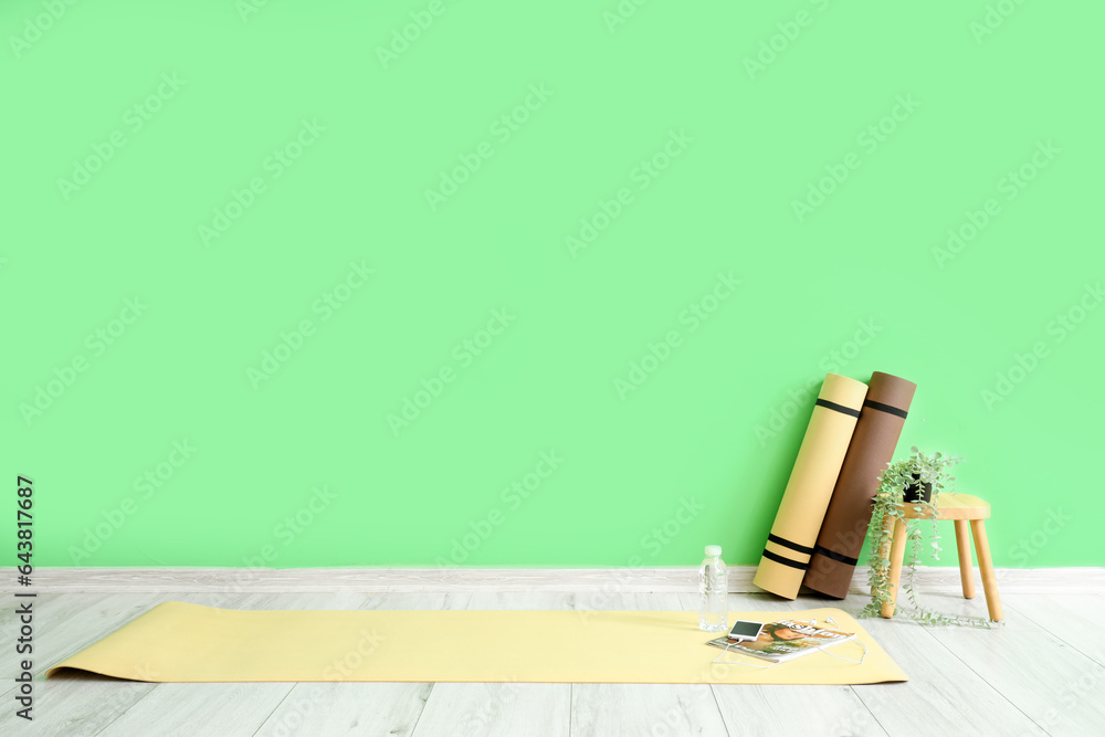 Fitness mats with mobile phone, magazine and stool near green wall in gym