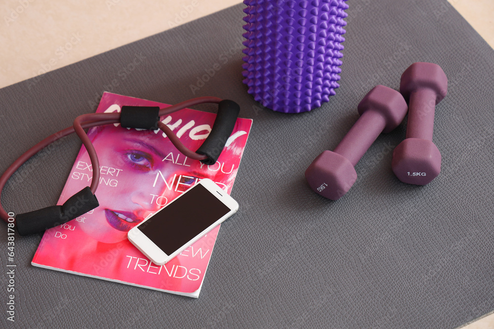 Sports equipment with mobile phone and magazine on fitness mat in gym, closeup