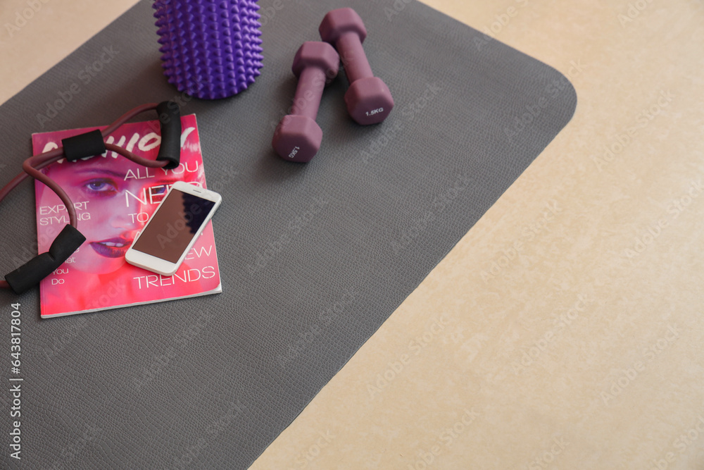 Sports equipment with mobile phone and magazine on fitness mat in gym, closeup