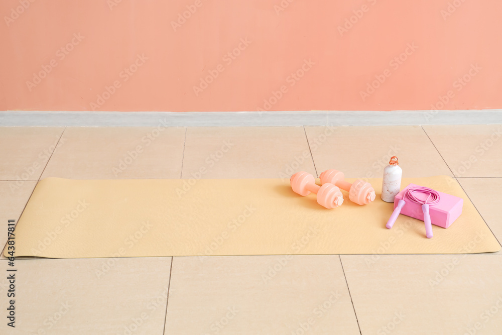 Sports equipment with bottle of water on fitness mat near pink wall in gym