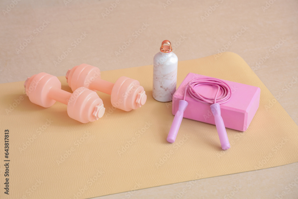 Sports equipment with bottle of water on fitness mat in gym