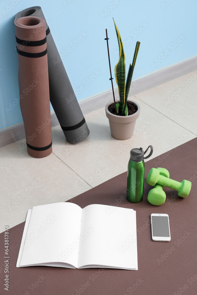 Blank magazine with mobile phone, dumbbells and bottle on fitness mat in gym