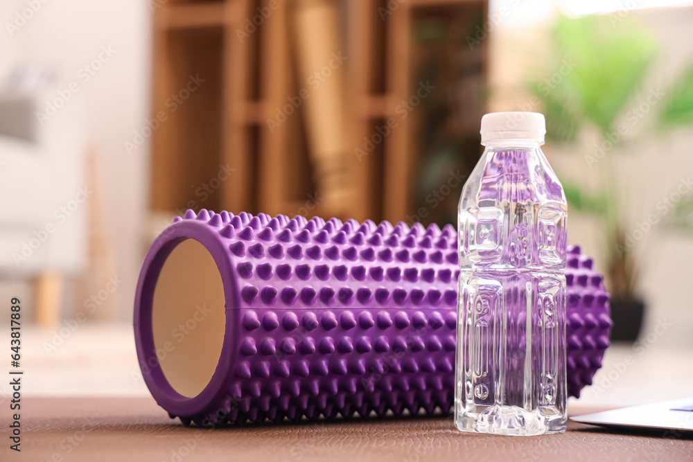 Bottle of water with foam roller on fitness mat in room