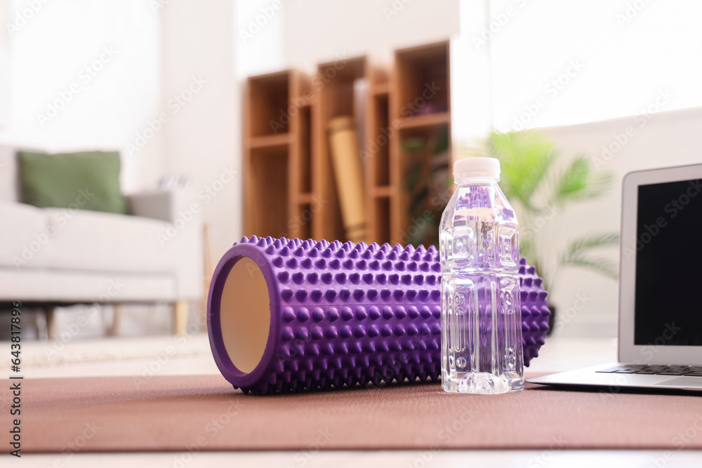 Bottle of water with foam roller on fitness mat in room