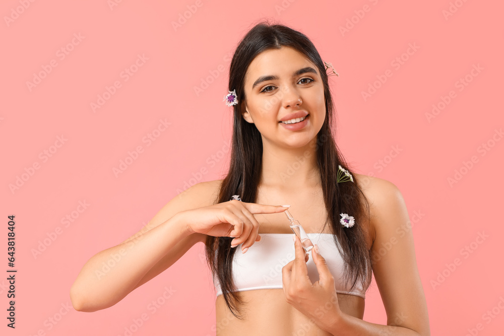 Beautiful young woman with flowers and ampule on pink background