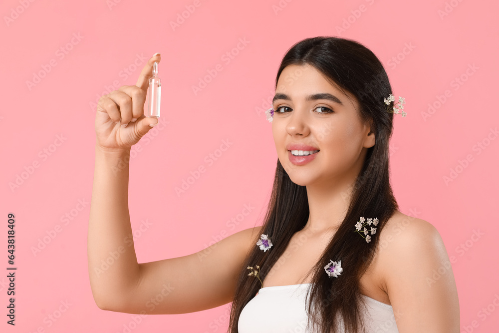 Beautiful young woman with flowers and ampule on pink background