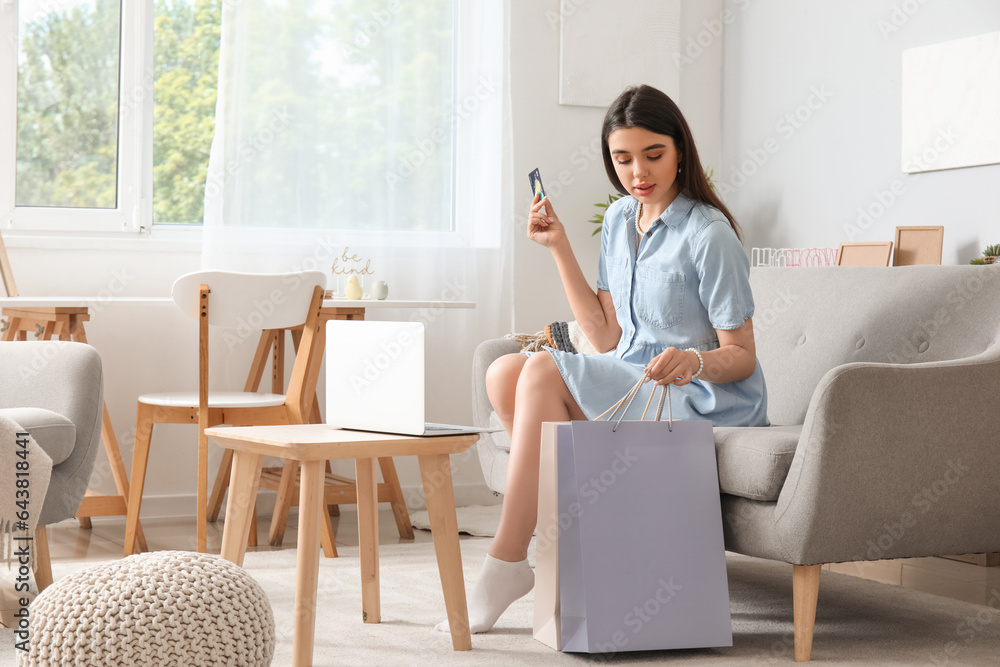 Young woman with credit card and shopping bags at home