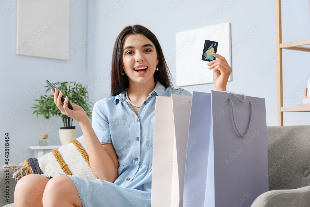 Young woman with credit card, mobile phone and shopping bags at home