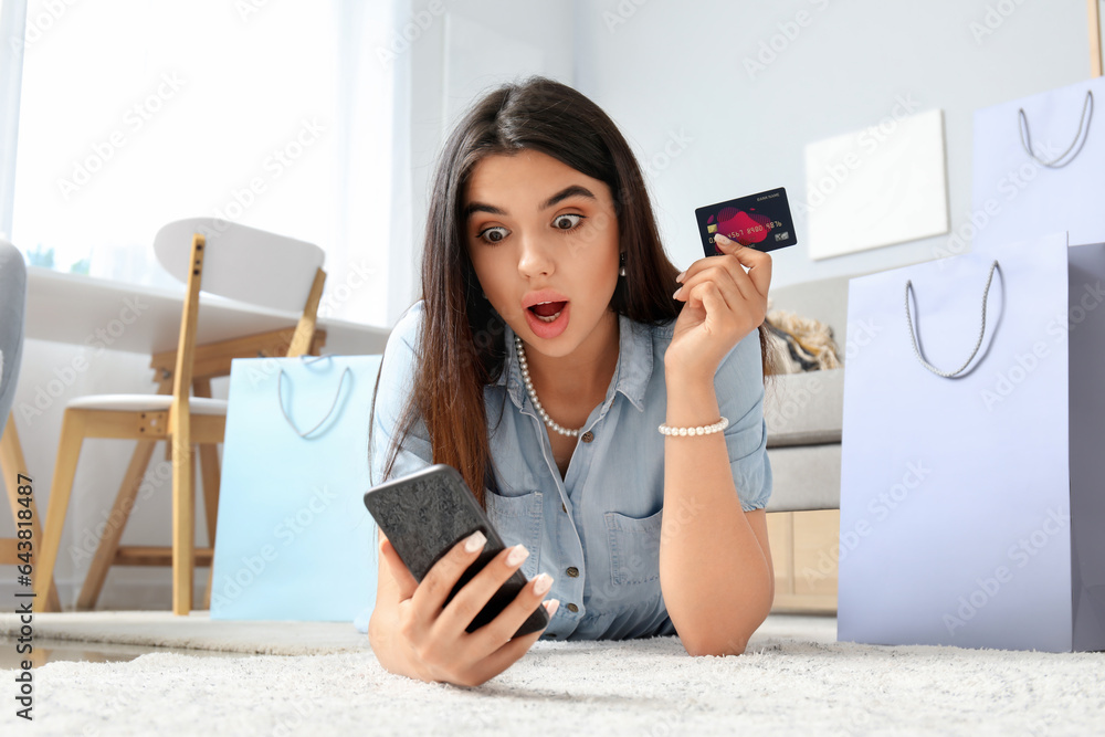 Shocked young woman with credit card and mobile phone shopping online at home