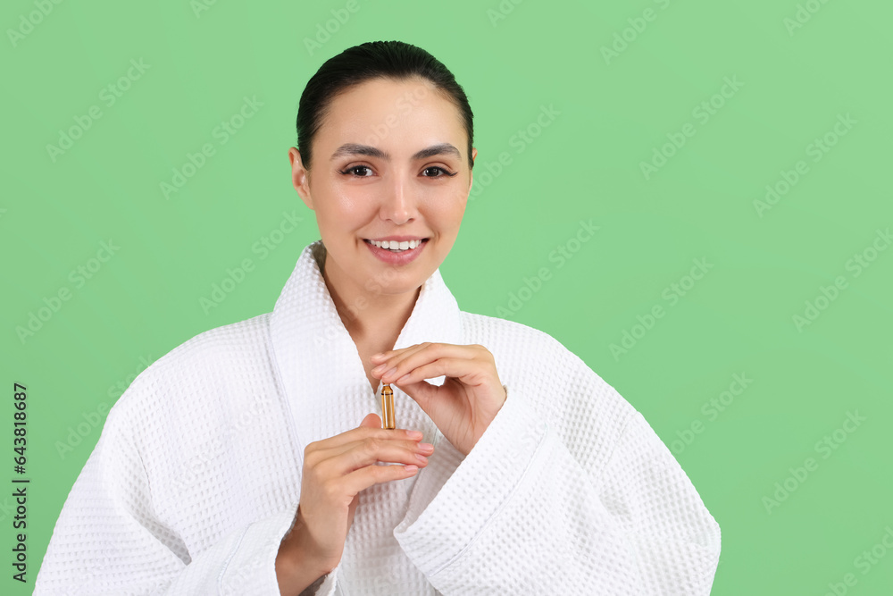 Beautiful young woman with ampule on green background