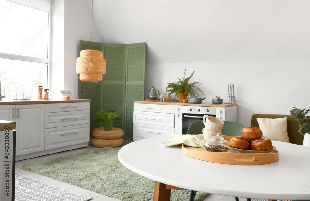 Dining table with cinnamon rolls, tea leaves and cups in modern kitchen